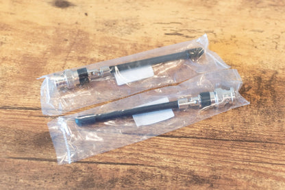 Two pens in clear plastic packaging on a wooden surface