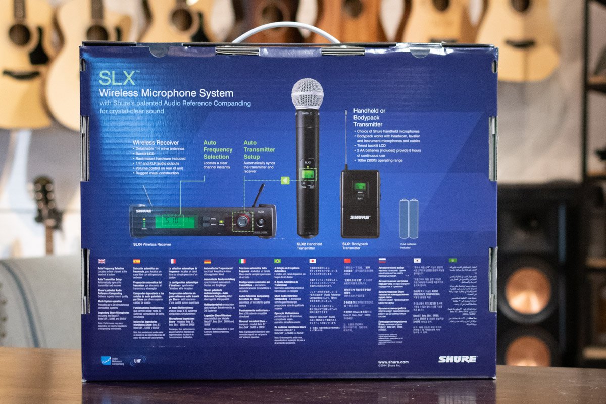 Shure SLX wireless microphone system packaging on a table with musical instruments in the background